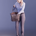 Woman Holding Brown Handbag With Patterned Interior Wearing Blue Shirt And Gray Pants Against Purple Background