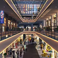 Bustling Evening Commercial Street with Shoppers Stores Hanging Lights Glass Facades and Green Plants