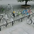 Colorful Bicycles Parked on Outdoor Bike Rack With Stone Pavement and Trees