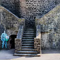 Medieval Castle Exterior With Stone Walls Stairs And Blue Costumed Figure Near Entrance