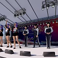 Group of young women performing on stage with bright stage lights and event backdrop