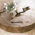 Round Metallic Coffee Table With Sculptural Indents And White Flower Arrangement On Wooden Floor