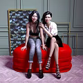 Two Women Sitting On Red Ottoman In Stylish Room
