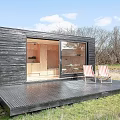 Black Detached House With Large Glass Windows And Lit Interior In Natural Surroundings