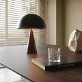 Minimalist Table Lamp With Black Shade On Wooden Table With Book Glass And Window Blinds