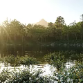Scenic Lake View With Sunlight Through Trees Mountain Backdrop And Calm Water Reflections