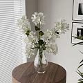 White Flowers With Green Leaves In Glass Vase On Wooden Round Table