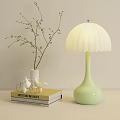 Light Green Table Lamp With White Pleated Shade Near Books And Vase With Twigs