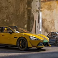 Yellow And Black Sports Cars Parked Against Weathered Stone Building Walls