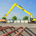Yellow Excavator Loading Truck At Construction Site With Trees And Blue Sky