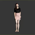 A woman wearing black top and pink skirt against gray background in standing pose