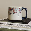 Ceramic Mug with Colorful Floral Patterns Butterflies and Blue Handle Placed On Stacked Magazines