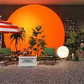 Outdoor Leisure Area With Orange Circular Backdrop Red White Striped Umbrella Green Chairs Plants And Moon Lamp