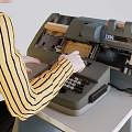 Game Movie Character Typing On Vintage Typewriter In Green Chair At Gray Desk