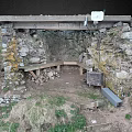 Outdoor Stone Structure With Wooden Beam Bench And Dirt Ground Surrounded By Grass
