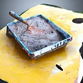 Yellow Tray With Blue Border Square Container Holding Gray Mixture And Wooden Handle Tool