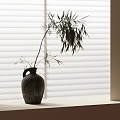 Dark Clay Vase With Bamboo Leaves On Light Colored Surface By White Blinds