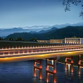 Illuminated Bridge At Night Spanning Water With Mountain Backdrop And Tree Branches