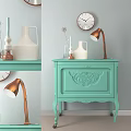 Light Green Chest of Drawers with Carved Decoration Brass Lamp White Vase and Wall Clock