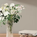 Transparent Glass Vase With White Flowers Green Leaves Against Light Gray Wall And White Book