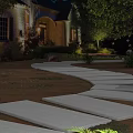 Nighttime Residential Garden Landscape With Curved Stone Walkway Lighting Greenery And Flower Beds