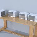 Four White Microwaves Placed On Wooden Long Table With Light Colored Wall Background
