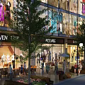 Bustling Commercial Street With Shop Windows Pedestrians Outdoor Seating Trees And Lighting