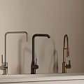 Three Different Colored Kitchen Faucets Silver Black Gold on Light Countertop with Beige Wall