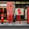 Woman Sitting On Red Bench Near Red Telephone Booth And Postbox By Brick Building