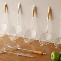 Stainless Steel Skimmers With Wooden Handles Hanging On Wall And On Countertop With Green Apples