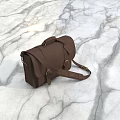 Brown Leather Briefcase with Adjustable Shoulder Strap Attached Tag and Metal Buckles on Marble Surface