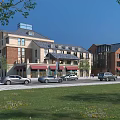 Vibrant Commercial Street with Modern Traditional Buildings Red Awnings Parked Cars and Green Lawns