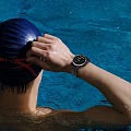 Person Wearing Waterproof Smartwatch Adjusting Swim Cap In Blue Pool Water