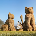 Large Straw Cat Sculptures Art Installation With People On Grassland Under Blue Sky