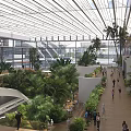 Modern Station Interior With Glass Roof Lush Plants Palm Trees Train And People Walking