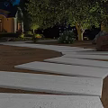 Nighttime Residential Garden Landscape With Curved Stone Walkway Lighting Greenery And Flower Beds