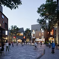 Vibrant Commercial Street with Pedestrians Trees Cafes Buildings and Evening Lighting