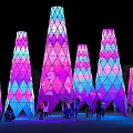 Colorful Geometric Illuminated Towers Stand At Night With People Gathering Around