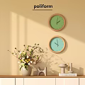 Two Round Wall Clocks with Green Light Blue Dials and Wooden Frames on Beige Wall