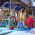 Decorative Teal Tram In Indoor Mall With Columns And Pedestrians Around