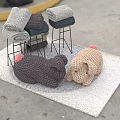 Knitted Pig Dolls In Gray And Beige On A Soft Carpet With Stacked Knitted Items