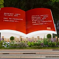 Red Open Book Sculpture with Text Surrounded by Green Plants and Bushes