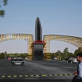 JINHE Entrance Gate with Golden Curved Design and Cars Pedestrians Under Blue Sky Trees