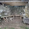 Outdoor Stone Structure With Wooden Beam Bench And Dirt Ground Surrounded By Grass