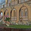 Elegant Garden Landscape With Yellow Building Arched Doors Balcony Greenery Lawn Planters And Wooden Deck