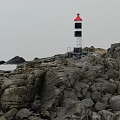 Red And Black White Lighthouse Tower Standing On Rocky Coastal Area
