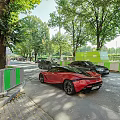 Red Sports Car Parked On Street With Green Fence And Trees