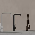 Three Different Colored Kitchen Faucets Silver Black Gold on Light Countertop with Beige Wall
