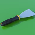 Household Putty Knife With Black Handle Yellow Connector And Silver Blade On Green Surface