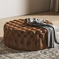Brown Round Tufted Ottoman with Gray Blanket on Patterned Rug and Wooden Floor